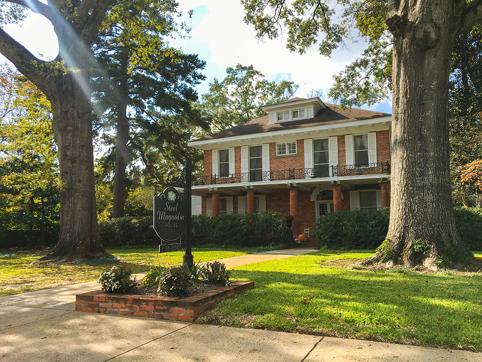 Exterior of the Steel Magnolia House surrounded by massive trees in Natchitoches.