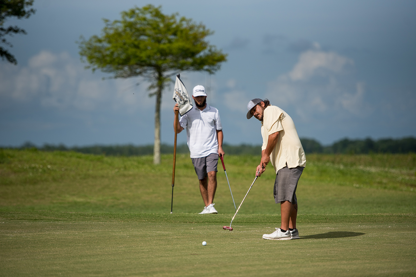 A man in a neon green golf polo takes a swing out of a sand trap at Wetlands Golf Course.