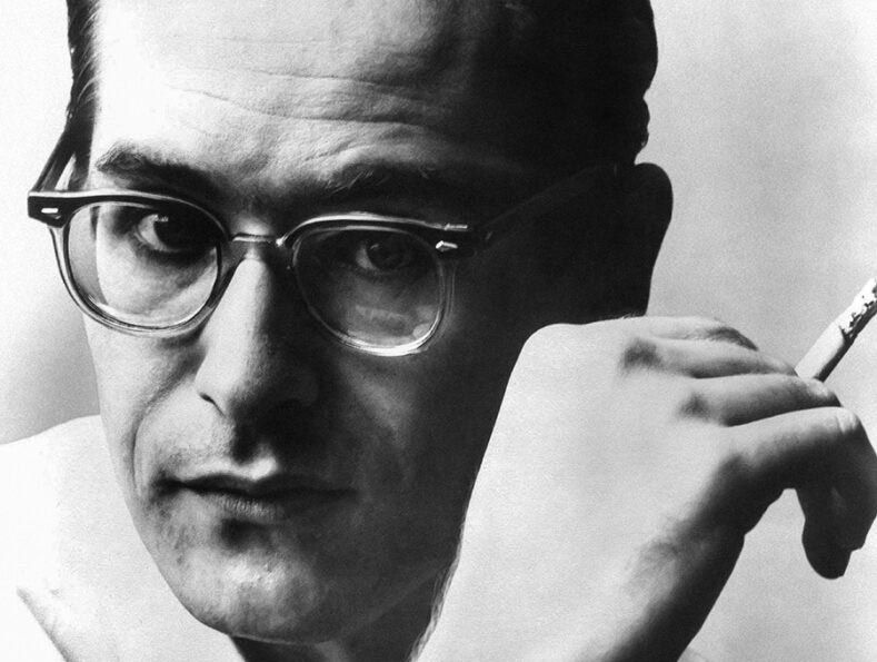 A portrait Bill Evans, wearing glasses and holding a cigarette