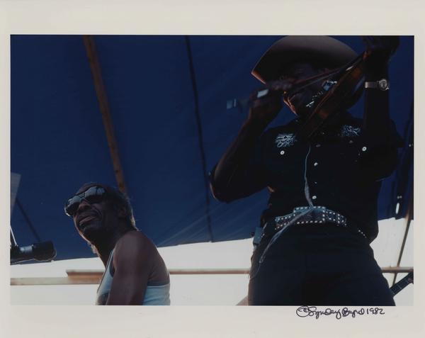 Professor Longhair performs in front of a royal blue backdrop. He wears a white cowboy hat.