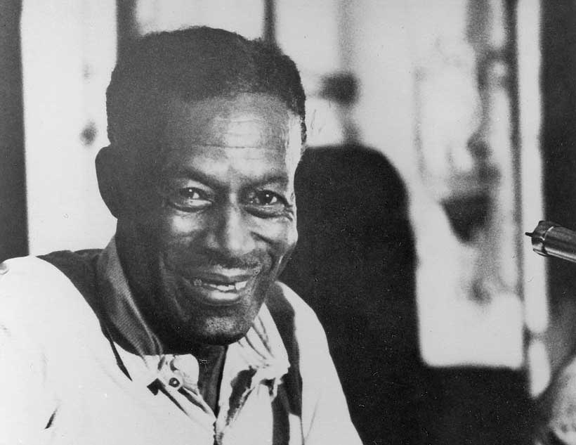 Son sites in a chair, holding his guitar, smiling to the camera