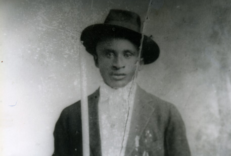 A black and white photo of Amede Ardoin dressed in a suit and jaunty hat