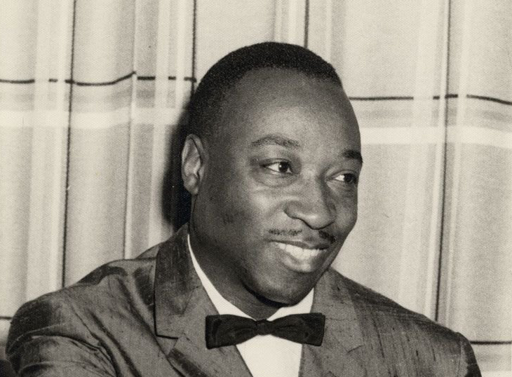 Musician Dave Bartholomew smiles and looks to his left while sitting in a chair in a tux