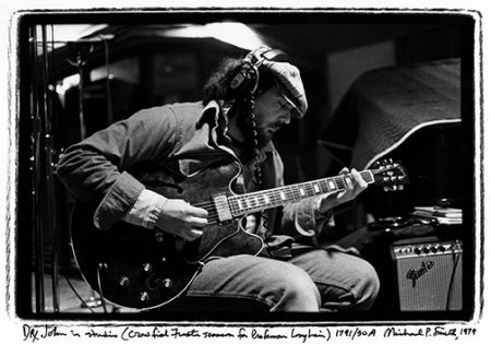 Dr. John holds a guitar and wears headphones in a recording studio