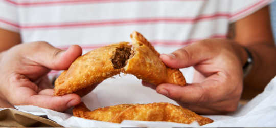 Hands break apart a perfectly fried meat pie.