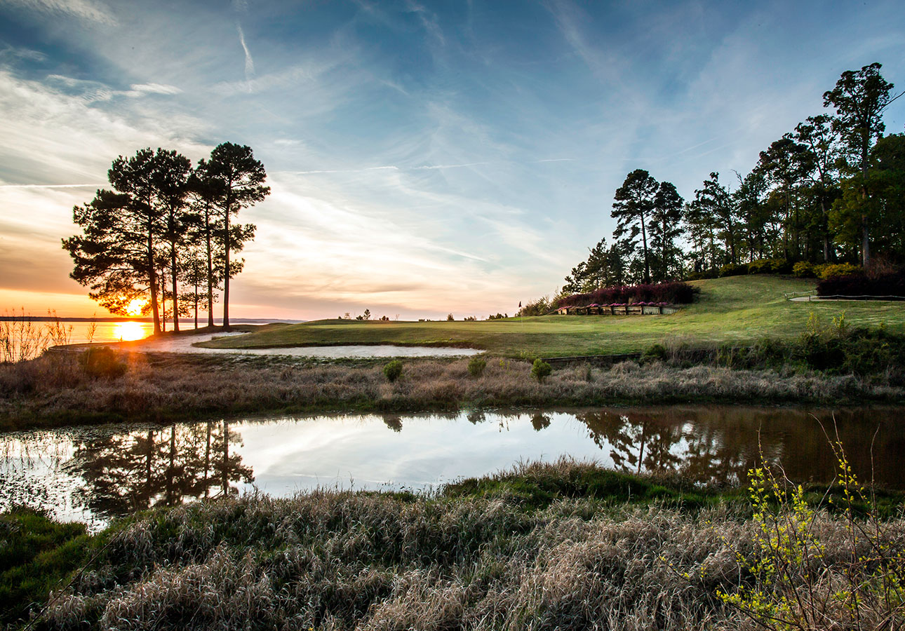 Cypress Bend Golf Resort at dusk, with a blue, slightly pink sky, with a pond and tall trees in the background.