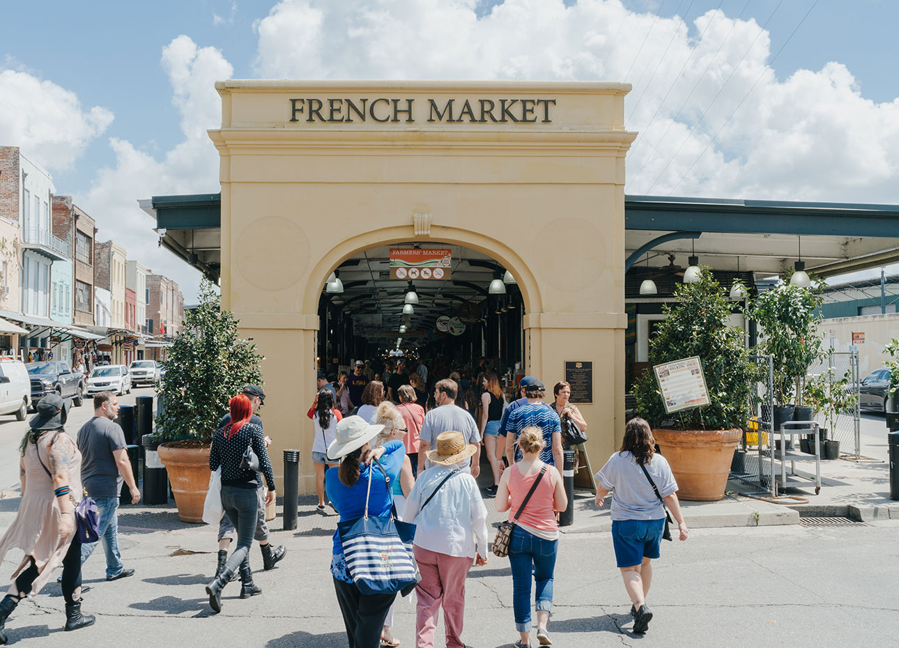 A large archway making the entrance to the French Market in New Orleans, Louisiana, surrounded by people shopping.