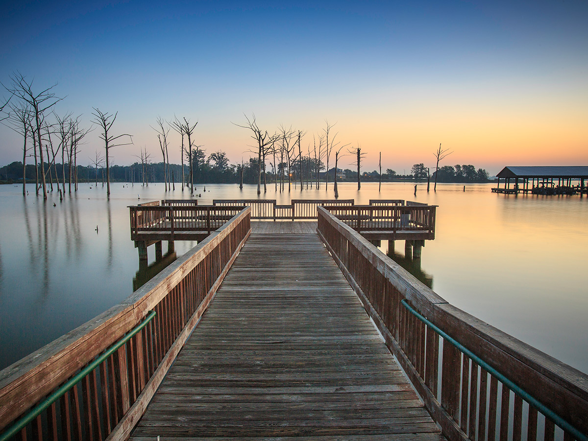 A wooden fishing dock stretches into the blue waters of Poverty Point Reservoir State Park.