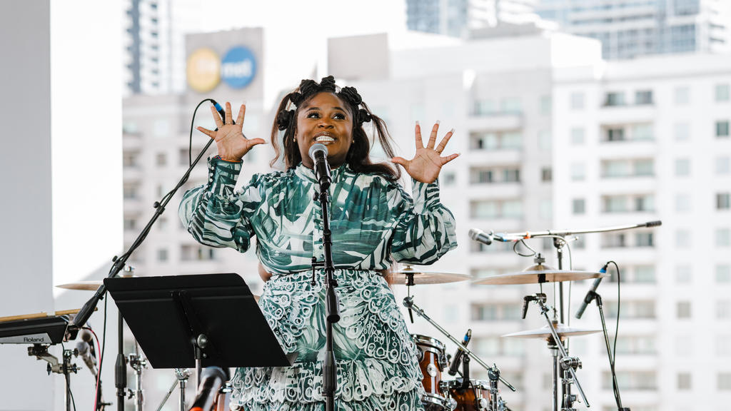 A performer smiles and gestures before a crowd.