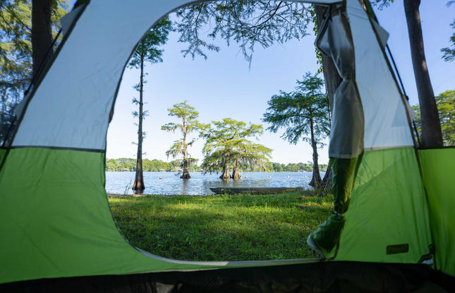 The flap of a green and blue tent opens up to reveal a beautiful lake with trees jutting out of the water at Lake Bruin State Park.