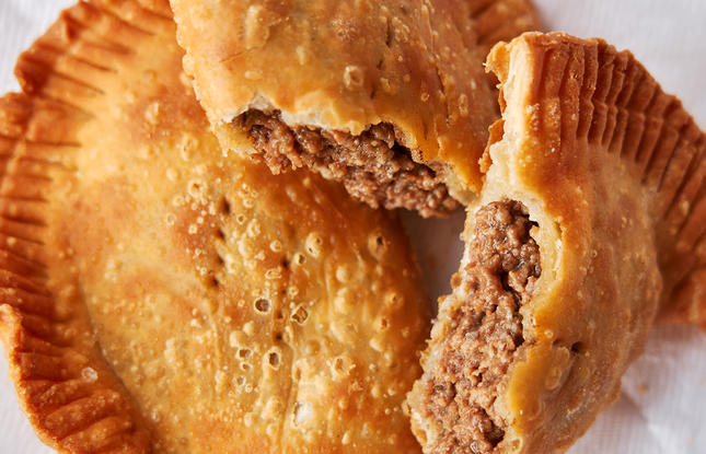 A perfectly fried, deliciously flaky meat pie, ripped in half to reveal buttery crust surrounding seasoned ground meat.