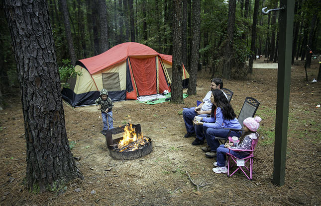 A family’s campsite at Lake D'Arbonne State Park, featuring several chairs, a roaring fire and their tent in the background.