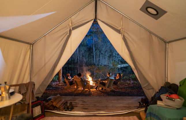 A group of people enjoying a bonfire, shot from the interior of a large tent at Fontainebleau State Park.