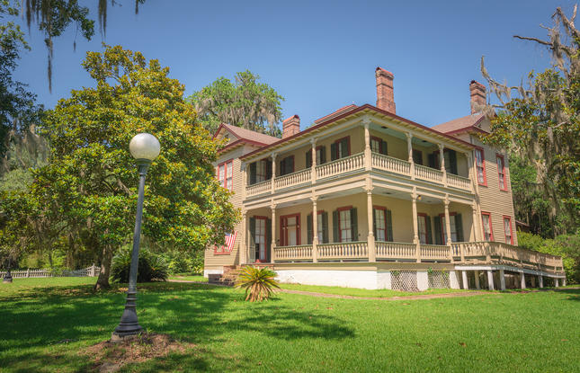 Exterior of the Otis House at Fairview-Riverside State Park, surrounded by towering trees and well-trimmed grass.