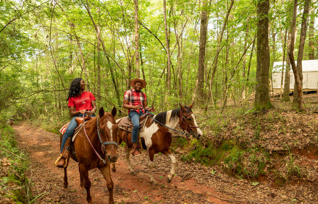 Two people ride horses through a dirt trail at Bogue Chitto State Park.