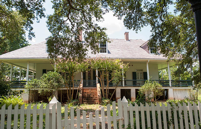 The main house at Oakland Plantation, Cane River Creole National Historical Park, framed by flowering trees and a white picket fence.
