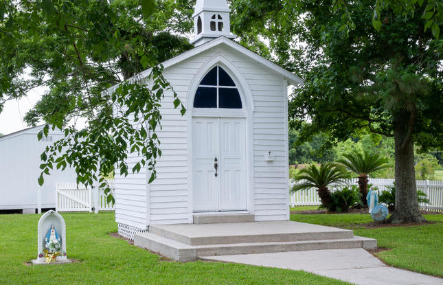 Small white chapel with a steeple surrounded by green grass and trees
