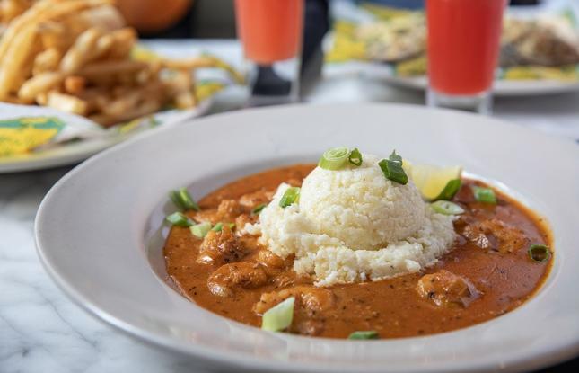 A plate of gumbo, dark in color, with rice and thinly sliced green onions on top.