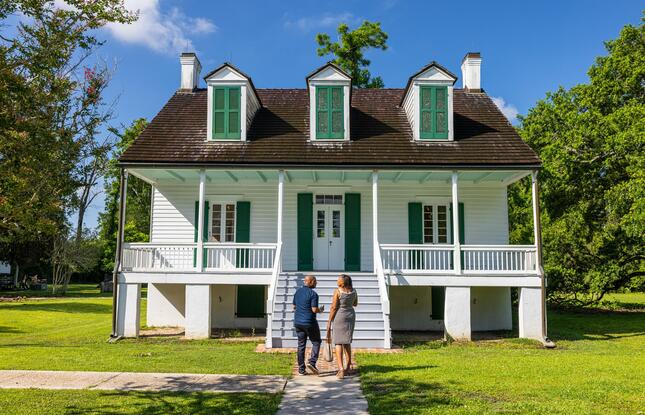 A couple stands in front of the home at E.D. White Historic Site, a white building with green shutters.