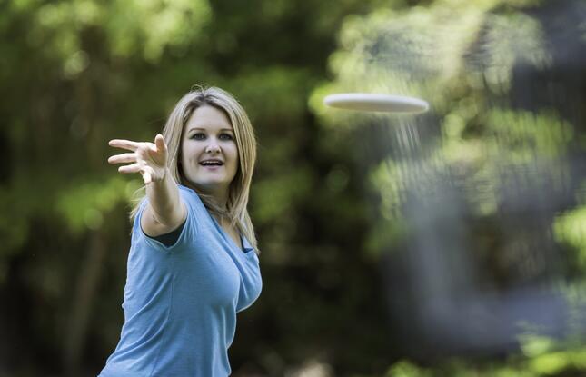 A woman in a blue shirt throws a white disc toward the camera.