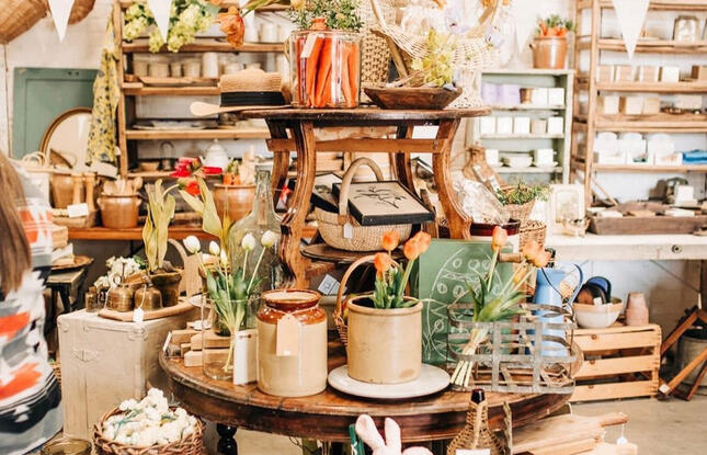 A cozy indoor display at Vintage Market Days featuring rustic wooden shelves, pottery, baskets, fresh tulips and curated vintage home décor items.
