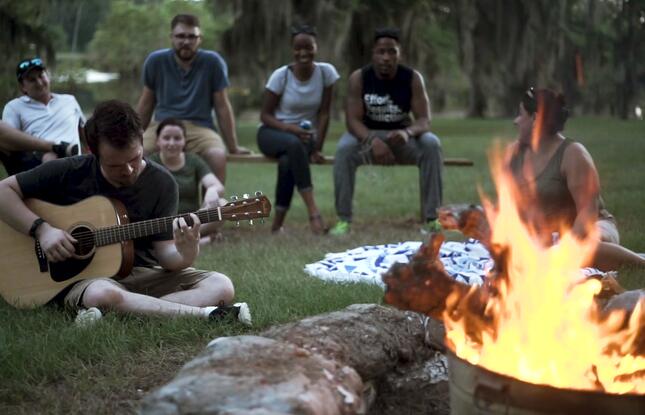 A man strums a guitar near a campfire