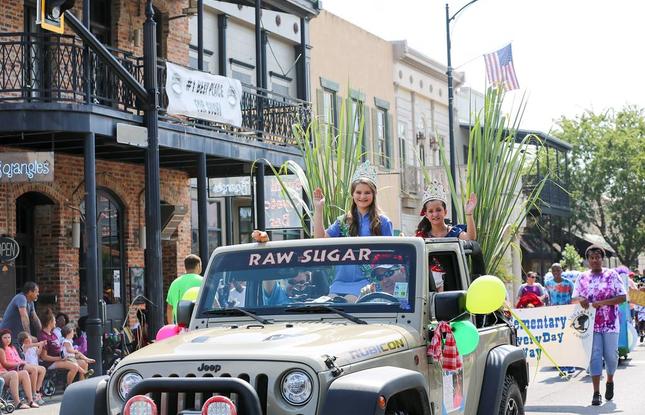 Two girls wearing crowns ride in a gray Jeep through the streets of downtown New Iberia during the Louisiana Sugar Cane Festival parade.