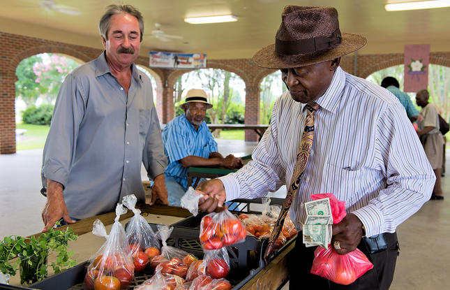 A vendor and shopper holding bags of apples at the Opelousas Farmers Market in Louisiana.