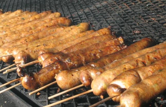 Boudin sausage on a stick, roasting over an open grill.