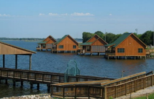 Wooden cabins at Poverty Point Reservoir State Park, situated off a boardwalk on the water.