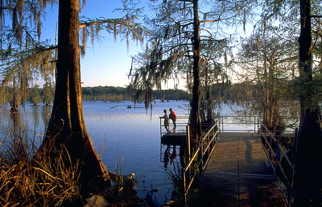 A couple stands at the edge of a pier, looking out at the water at Chicot State Park.