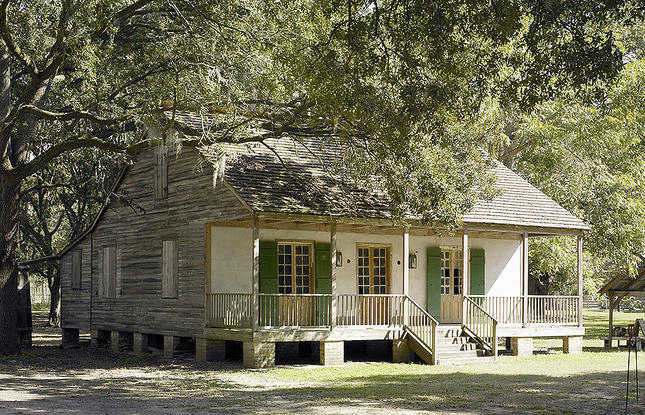 Preserved overseer’s cabin with white walls, wooden doors and green shutters surrounded by trees.
