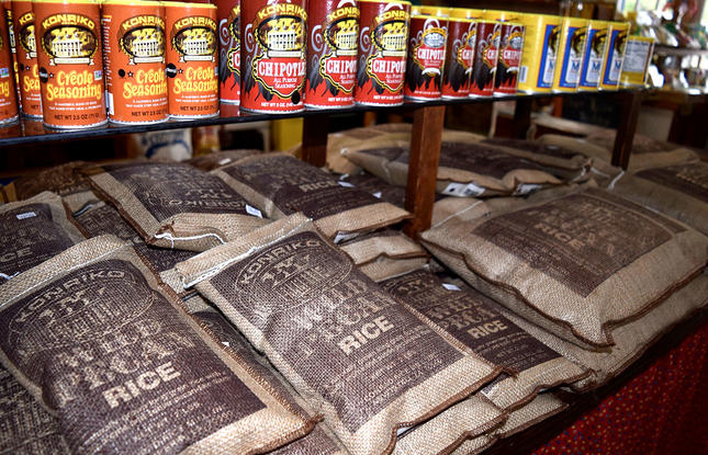 Bags of Conrad Mill Rice and bottles of Cajun seasoning by Konriko Spices in a dimly lit shop.