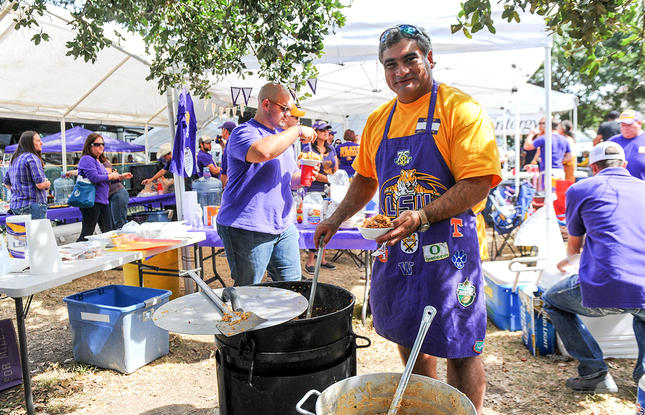 A man decked out in LSU Tigers merchandise stirs a large cast iron pot at a tailgate in Louisiana.