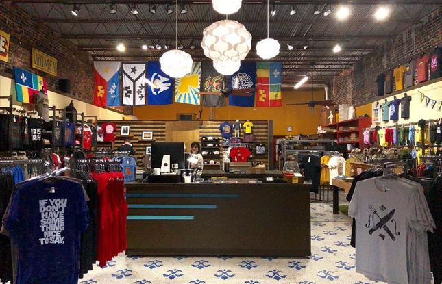 The interior of Parish Ink Store in Lafayette, featuring racks of quirky t-shirts and Louisiana sports flags hanging from the ceiling.