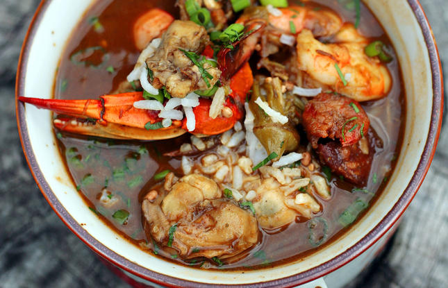 A red bowl piled high with seafood gumbo in a rich, tomato broth, with shrimp, crawfish and other seafood.
