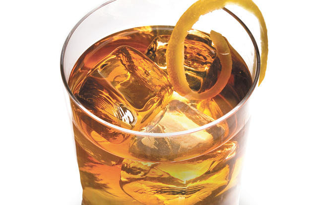 A golden-hued Vieux Carré cocktail with ice and a lemon twist, shown in a clear glass on a white background.