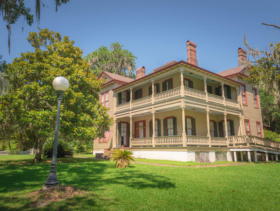 Exterior of the Otis House at Fairview-Riverside State Park, surrounded by towering trees and well-trimmed grass.