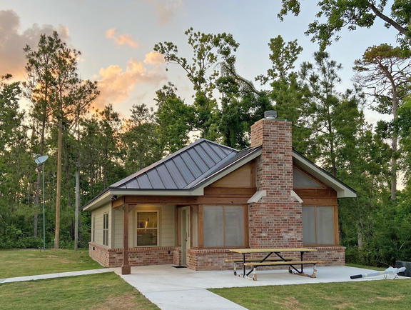 A mostly brick cabin at Sam Houston Jones State Park, with towering trees in the background and a light blue sky.