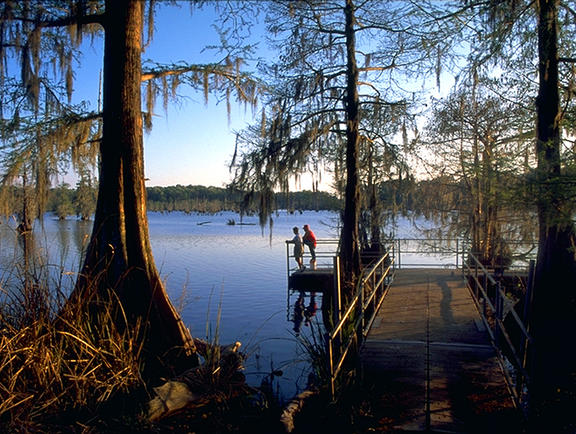 A couple stands at the edge of a pier, looking out at the water at Chicot State Park.