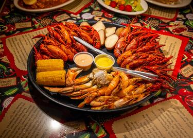 A large platter of seafood, including crawfish, corn and potatoes on a brightly decorated table at Boudreau &amp; Thibodeau’s Cajun Cookin’.