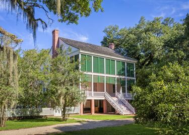 The Oakley House at the Audubon Historic Site, with bright green window panes, surrounded by lush green trees and shrubs.