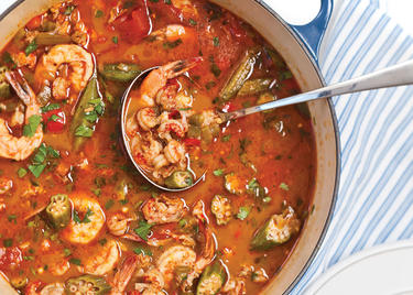 On a table in Louisiana, a silver ladle sits in a blue crockpot ready to scoop out red broth ladened with shrimp, crawfish, okra and spices.
