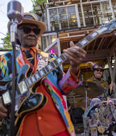 A Louisiana Musician wearing colorful jacket playing guitar