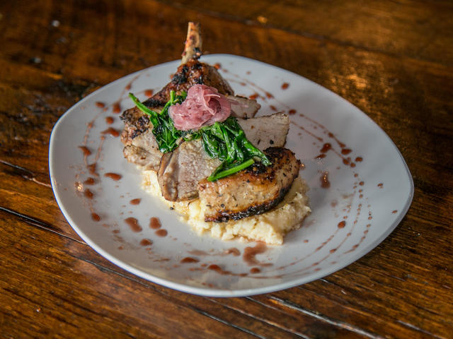 Bone-in Pork Chop over cheddar cheese grits with sautéed spinach and red wine butter sauce
