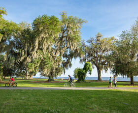 Two people ride bikes and two people jog along a paved trail on a sunny day at the Mandeville Lakefront. Credit: Louisiana Northshore