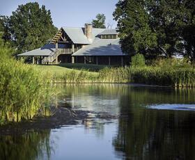 Black Bear Golf Club Lodge surrounded by large trees, on the shores of a calm lake.