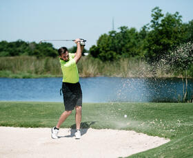 A man in a neon green golf polo takes a swing out of a sand trap at Wetlands Golf Course.