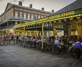 Outdoor view of the lively Cafe du Monde in New Orleans, Louisiana with people sitting at tables under a green canopy.