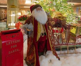 A Santa statue with a huge white beard and deep red coat, with arms outstretched next to a red mailbox.